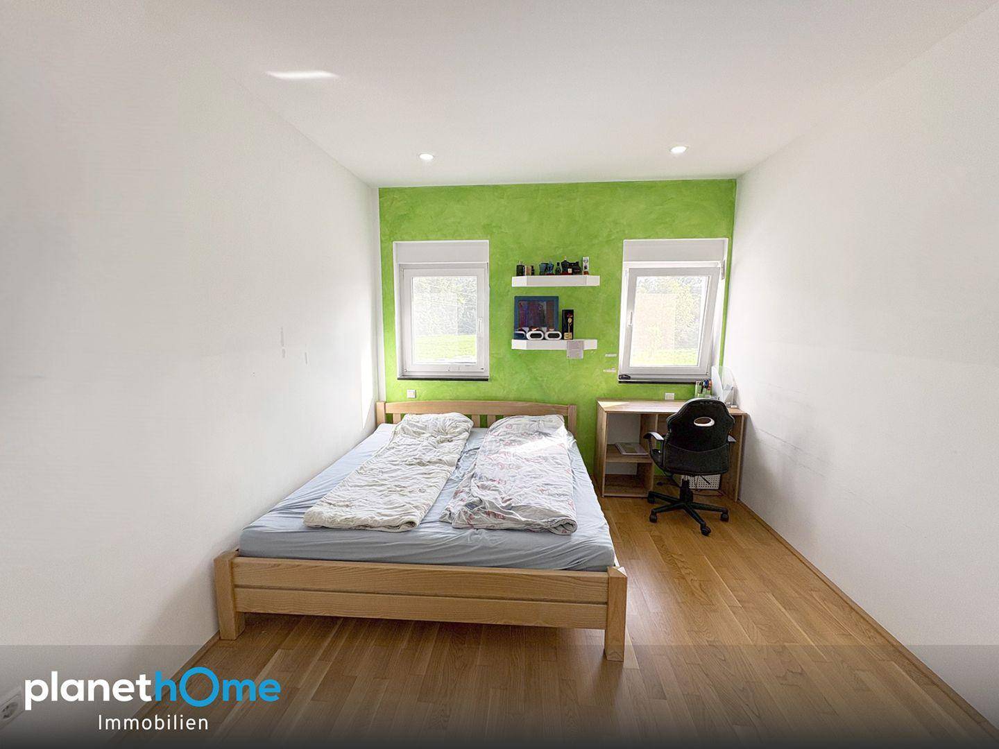 Helles Schlafzimmer mit Holzbett, Schreibtisch und einer auffälligen grünen Akzentwand.