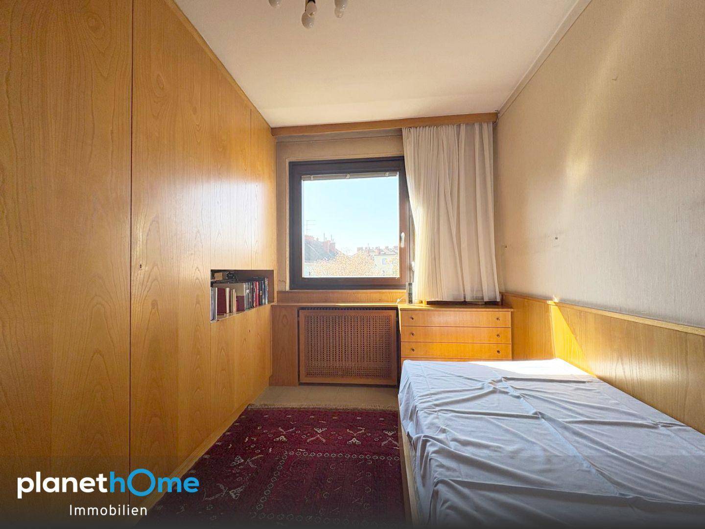 Kleines Schlafzimmer mit Holzvertäfelung, Einzelbett und Blick nach draußen.