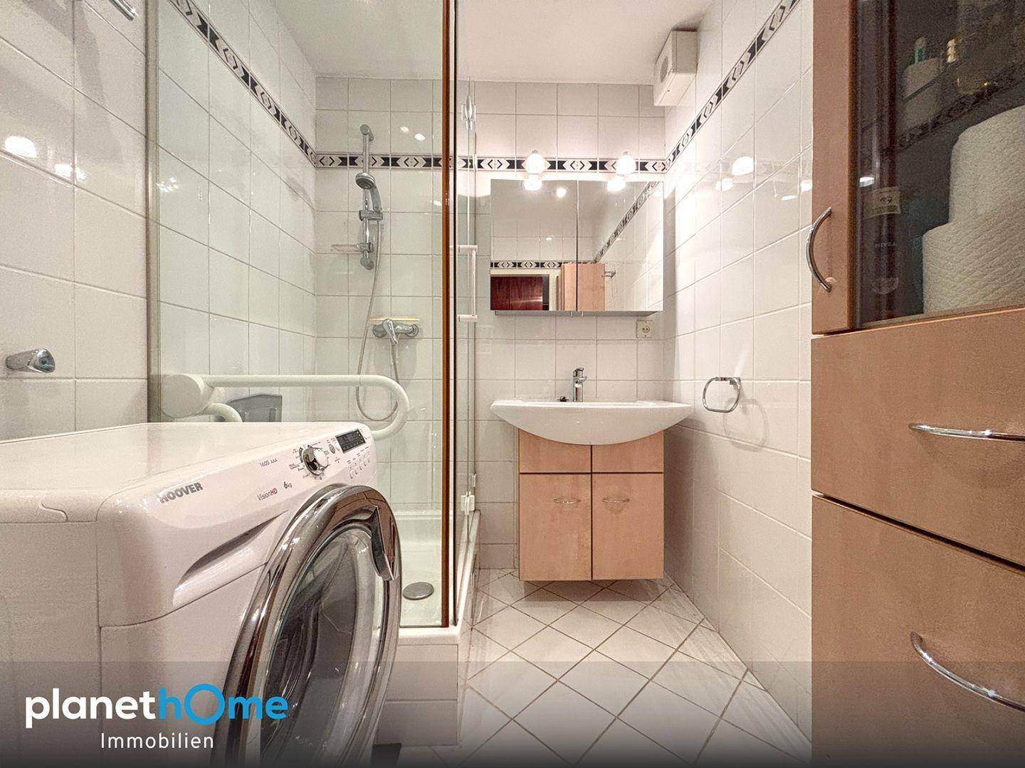 Badezimmer im älteren Stil mit Dusche, Waschmaschine und Haltegriffen für Barrierefreiheit.