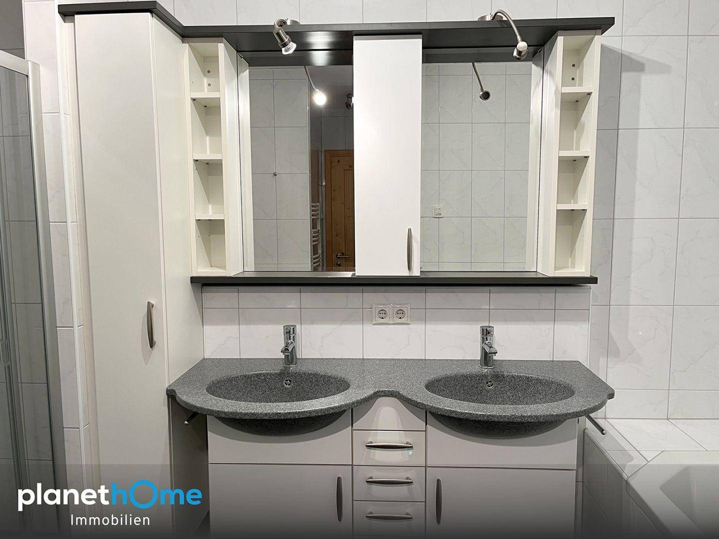Badezimmer mit Doppelwaschbecken, Spiegelschrank und hellen Fliesen an den Wänden.