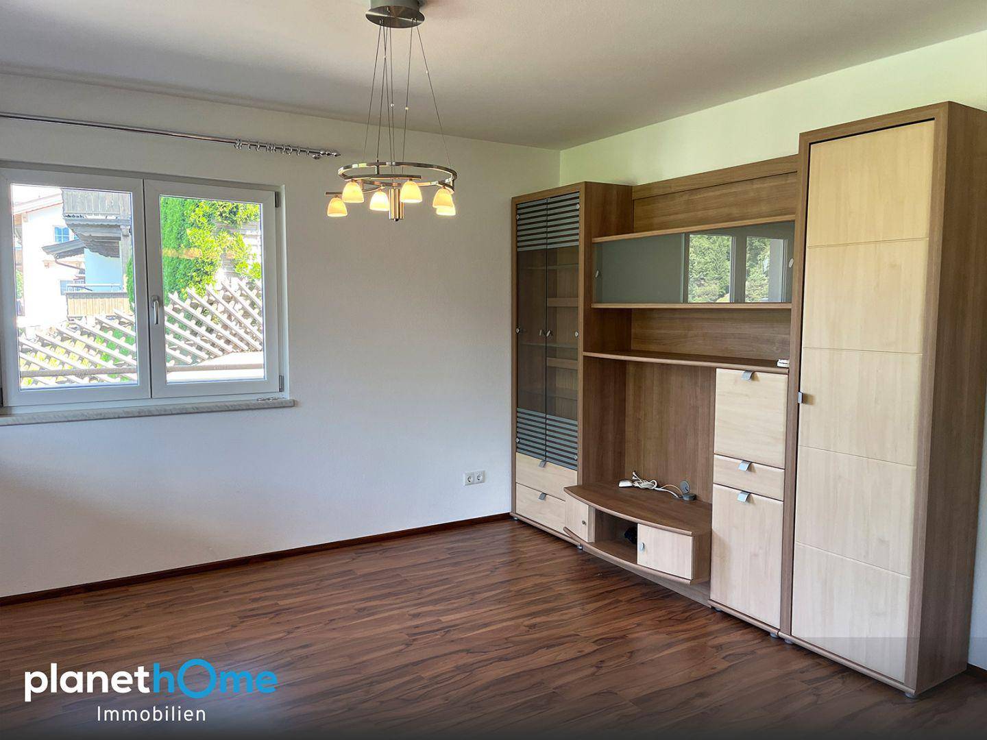 Geräumiges Wohnzimmer mit großer Holzschrankwand, Holzboden und Fenster.