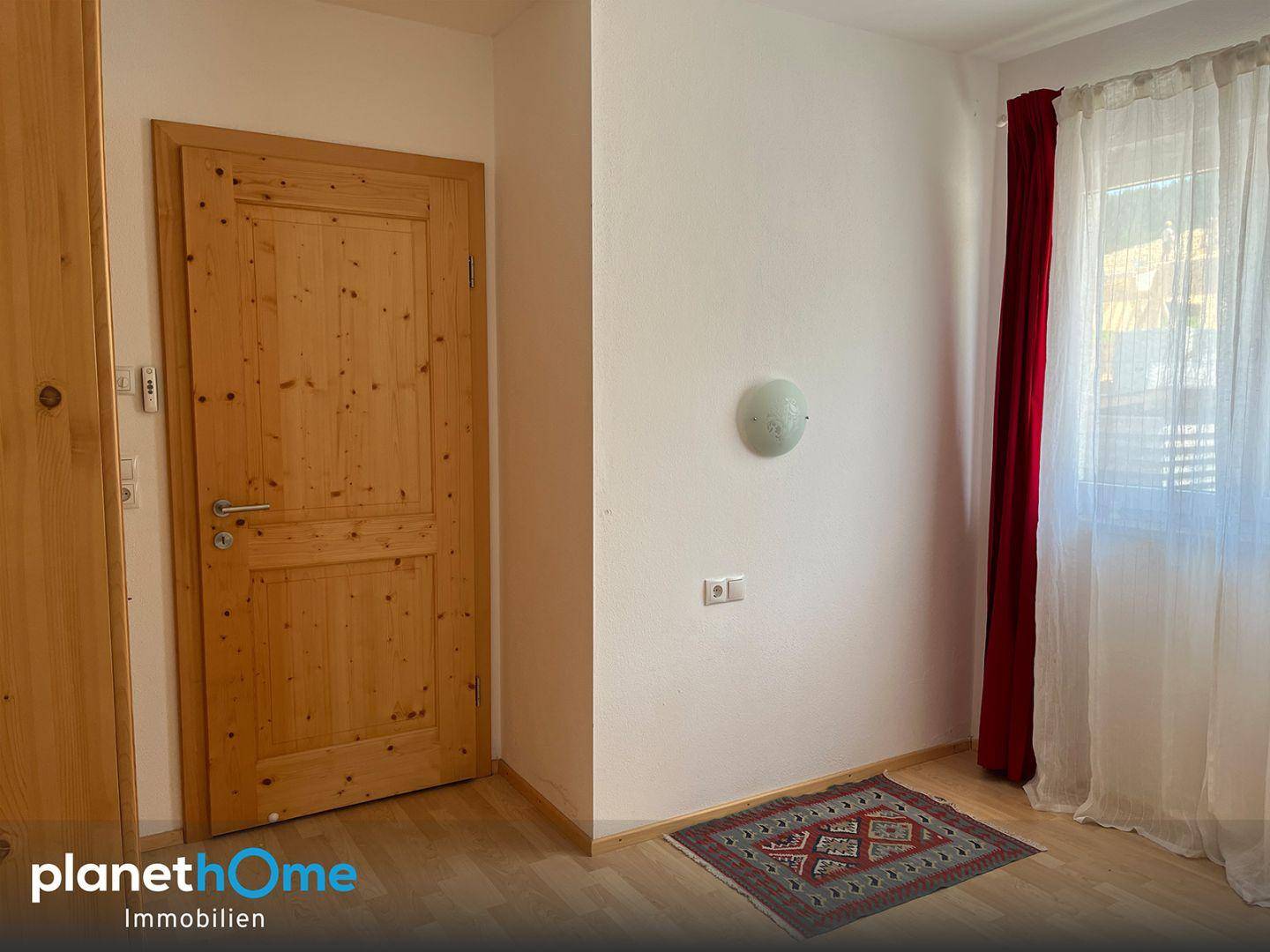 Heller Flur mit Holztür, Holzboden und einem kleinen Teppich.