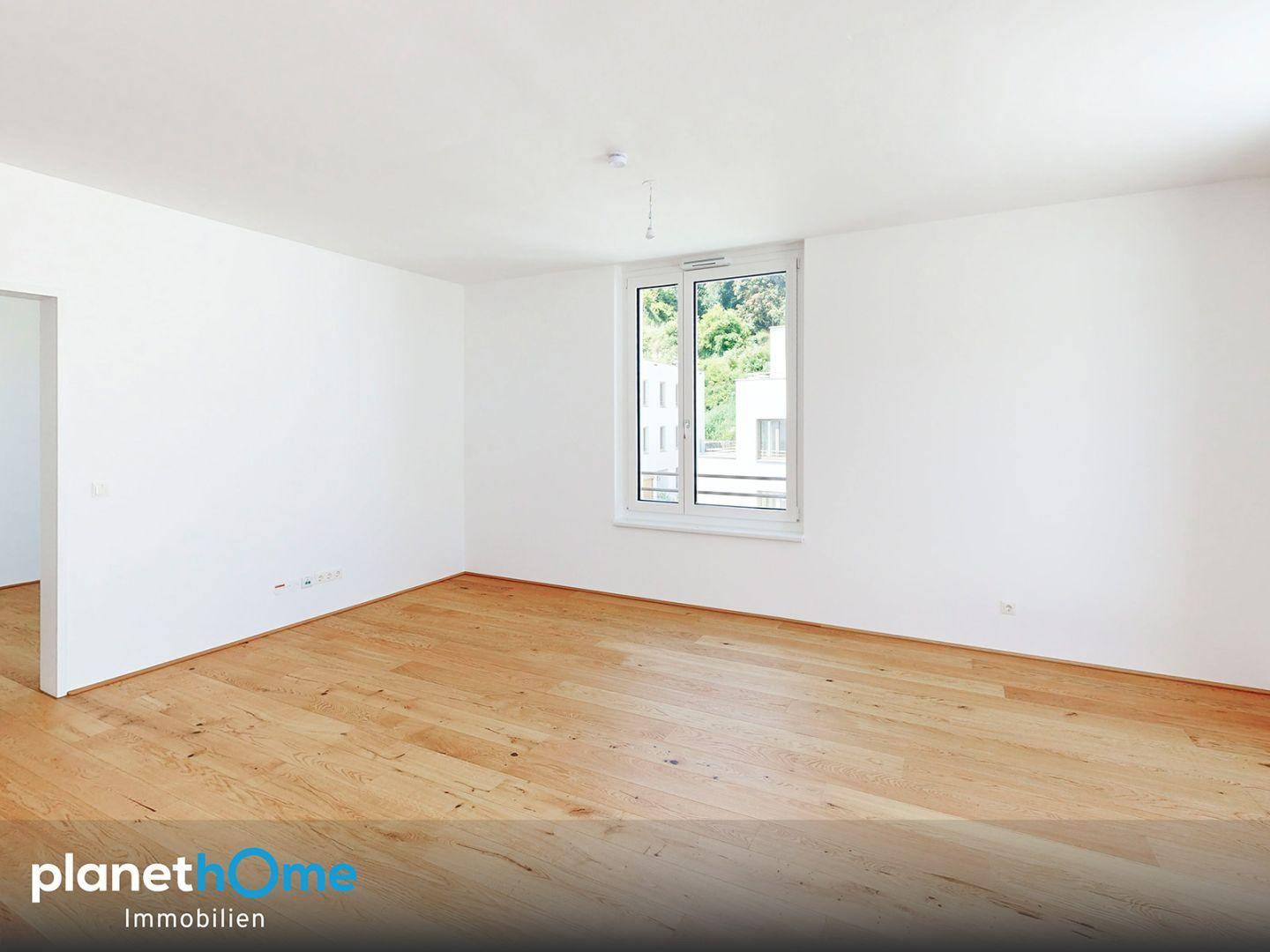 Geräumiges, unmöbliertes Zimmer mit hellem Parkettboden und einem großen Fenster.