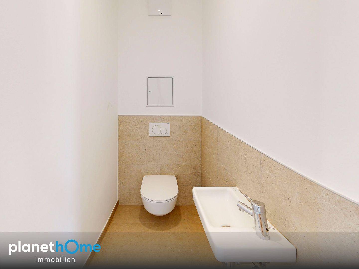 Separates WC mit wandhängender Toilette und kleinem Handwaschbecken.