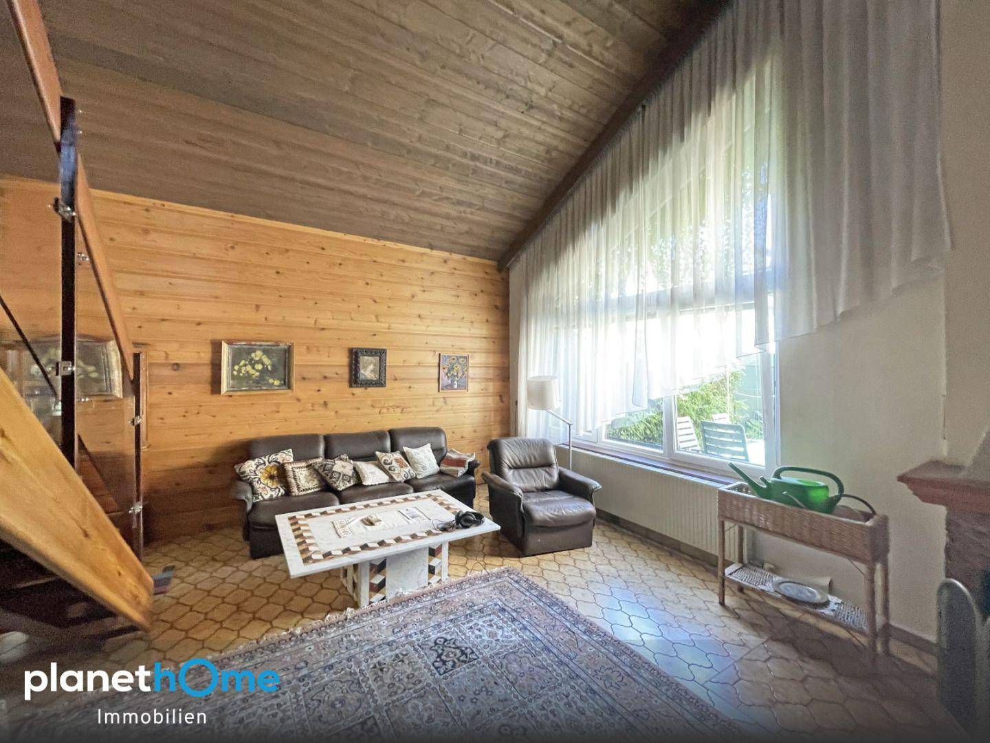 Rustikales Wohnzimmer mit Holzvertäfelung, hohen Decken und großem Fenster für viel Licht.