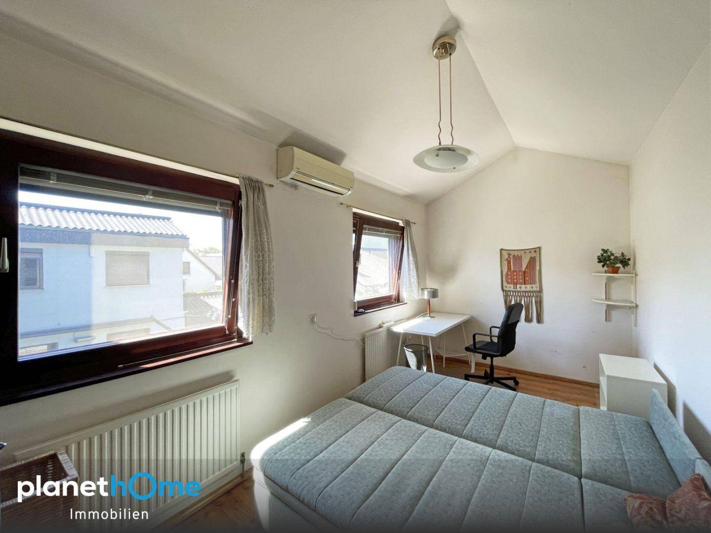 Helles Schlafzimmer mit Dachschräge, zwei Fenstern und Klimaanlage für angenehme Temperaturen.