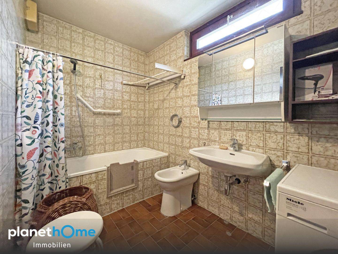 Badezimmer mit Badewanne, Bidet und Waschmaschine, gefliest im 80er-Jahre-Stil, gut erhalten.