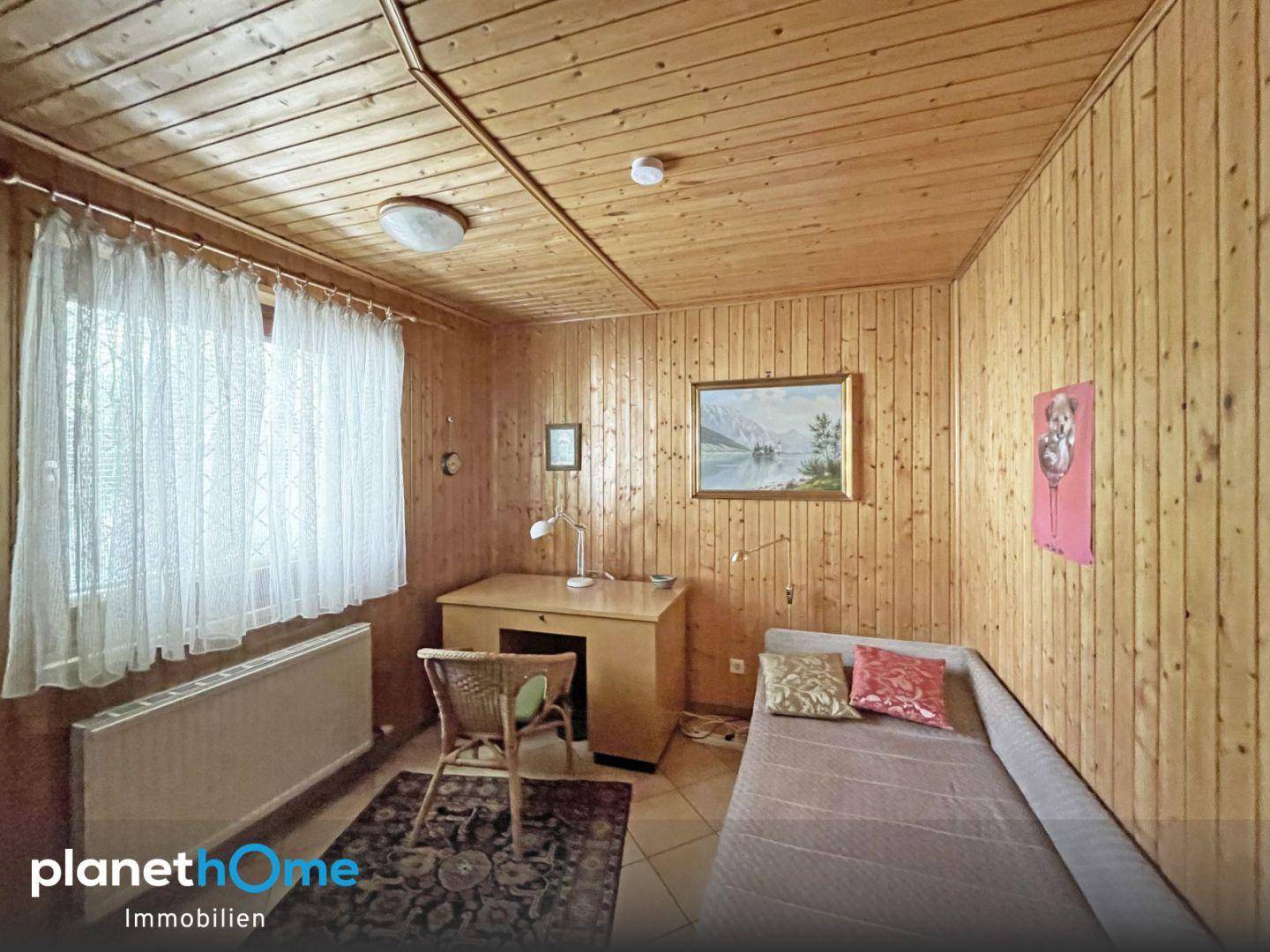 Kleines Zimmer mit Holzvertäfelung, Schreibtisch und Einzelbett, ideal als Gästezimmer oder Büro.