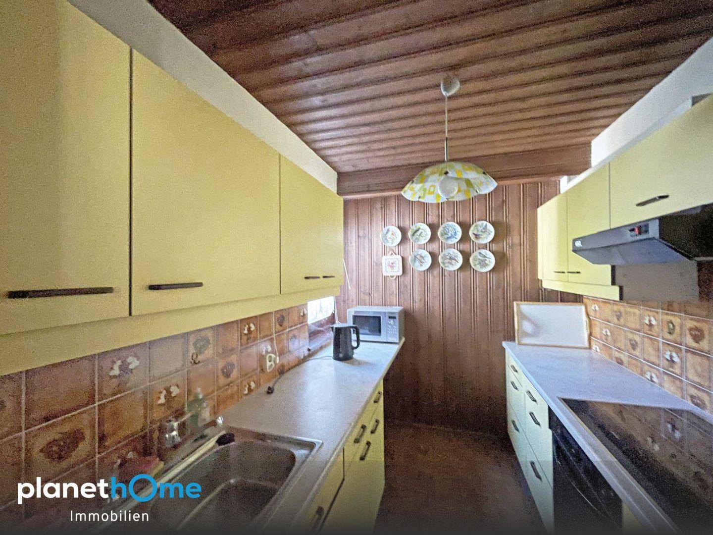 Küche im Retro-Stil mit gelben Schränken, Holzdecke und Fliesenrückwand, inklusive Mikrowelle.