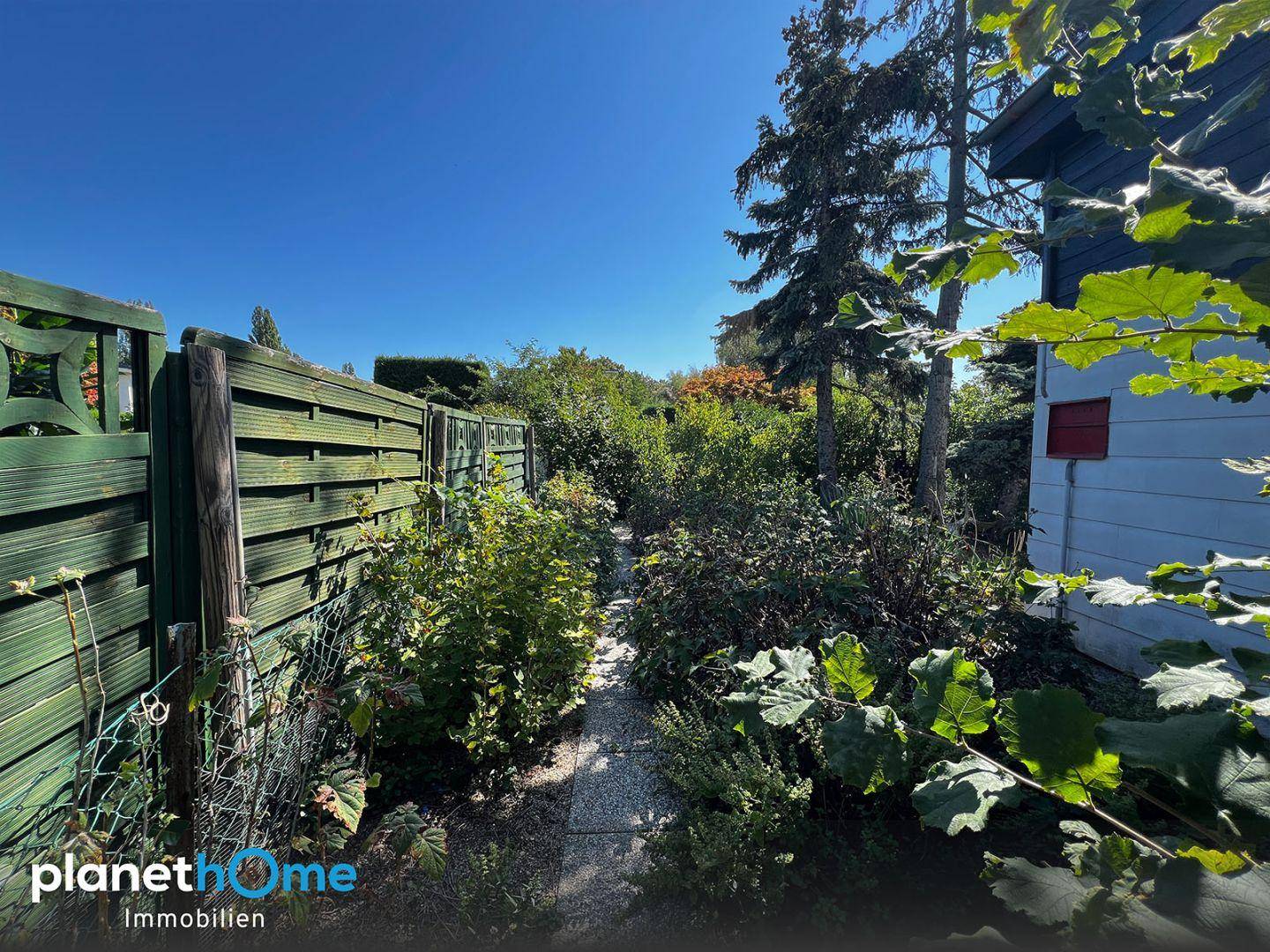 Schmaler Gartenweg umgeben von hohen Hecken und Bäumen unter blauem Himmel.
