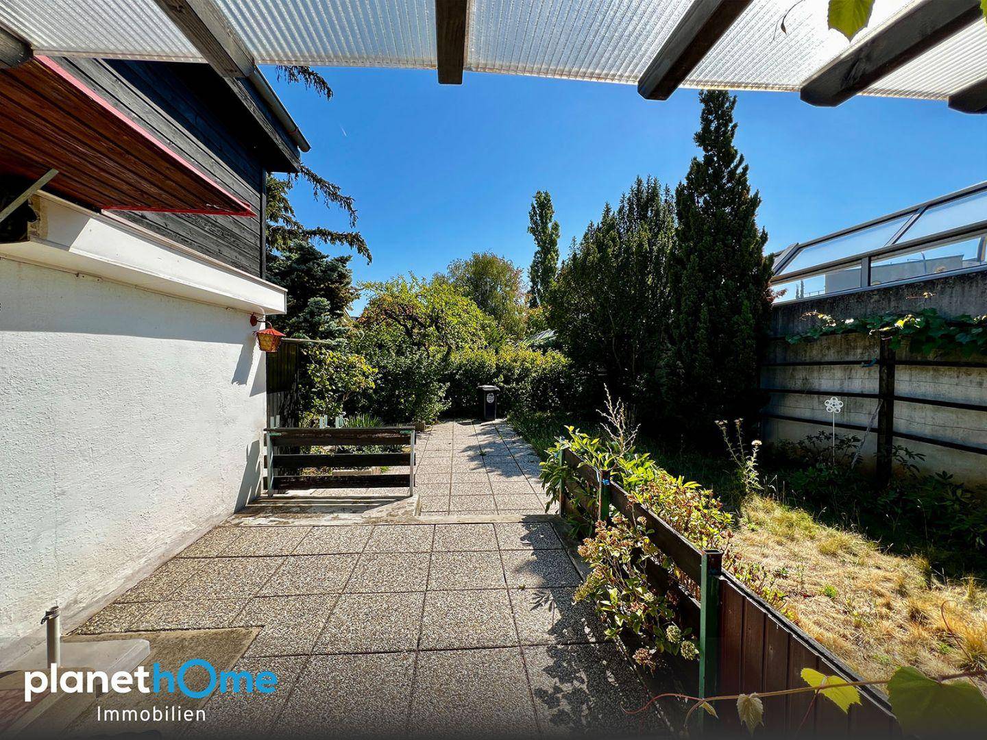 Gepflasterte Terrasse mit Überdachung und Zugang zu einem grünen Gartenbereich.