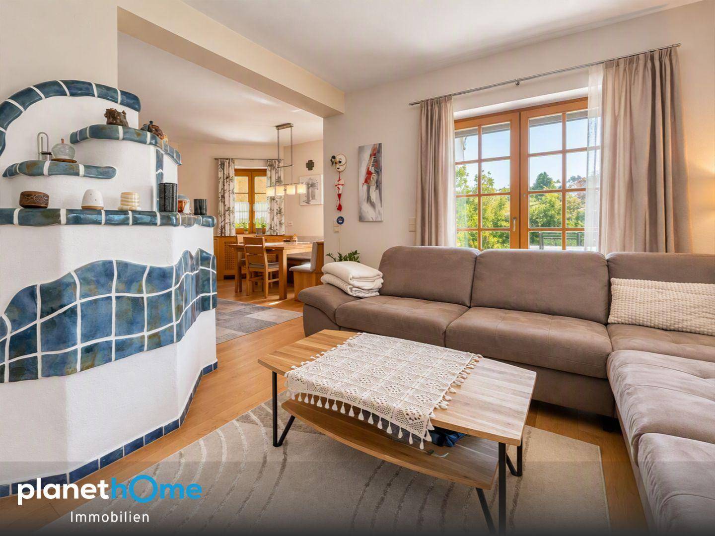 Heller Wohnbereich mit beigem Sofa, Kachelofen und Blick in den Essbereich.