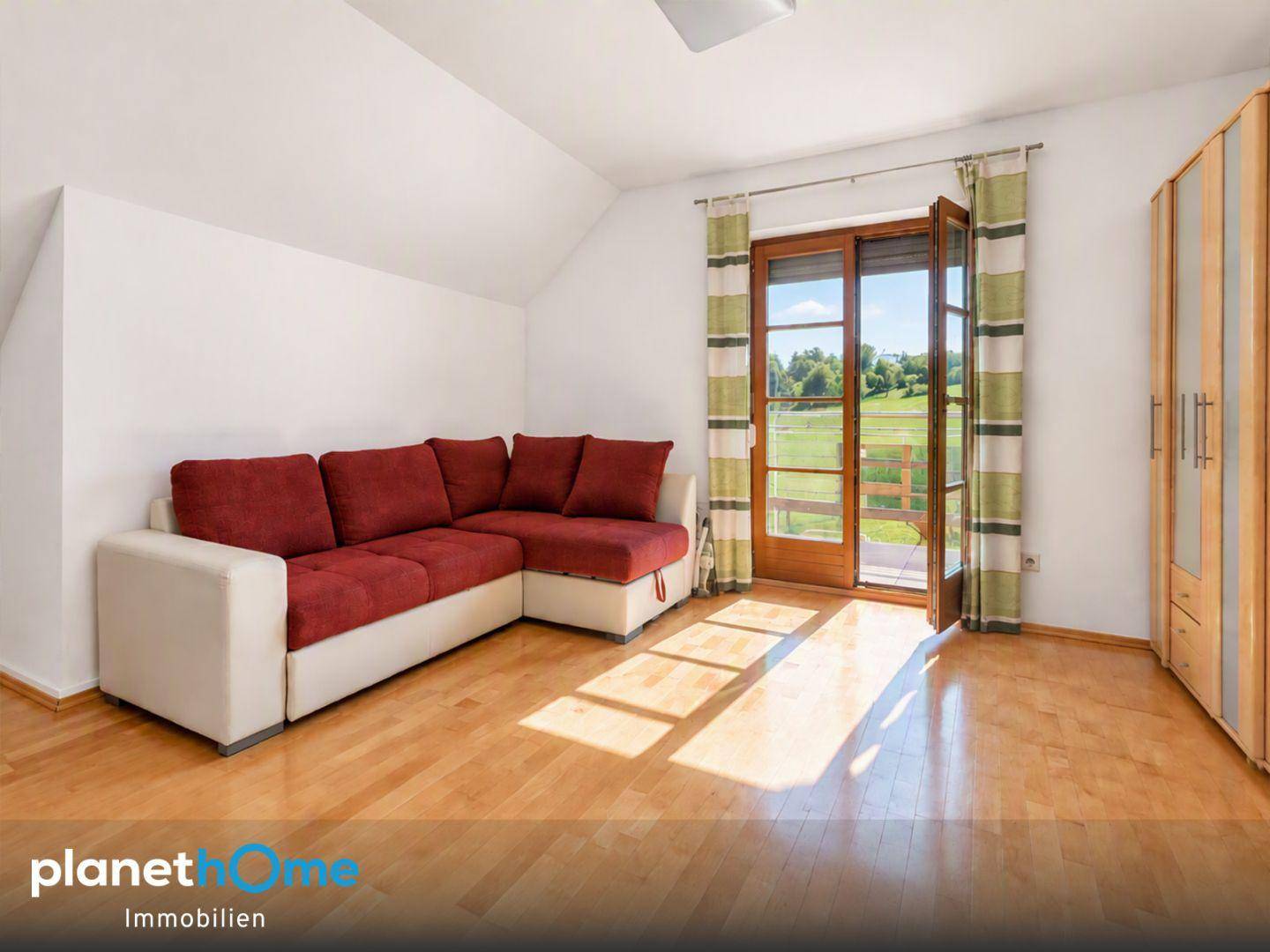 Helles Zimmer mit Holzboden, rotem Sofa und Zugang zu einem Balkon.