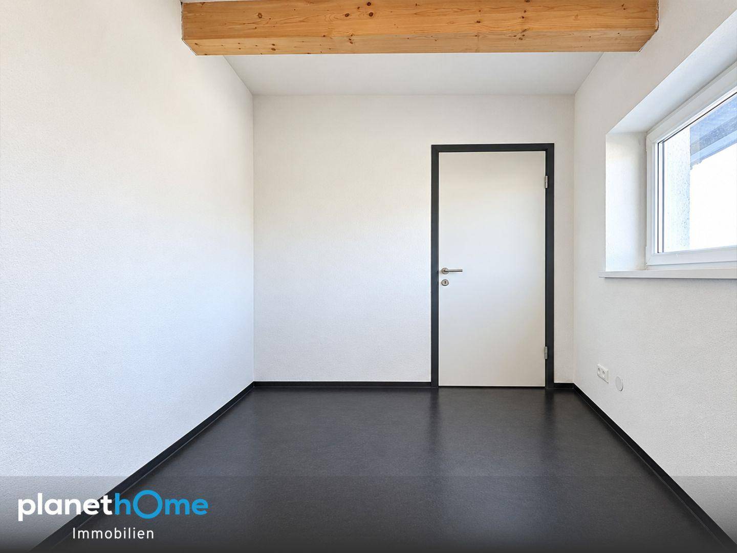 Kleiner Raum mit dunklem Boden, einem Holzbalken und einem Fenster, ideal als Ankleidezimmer.