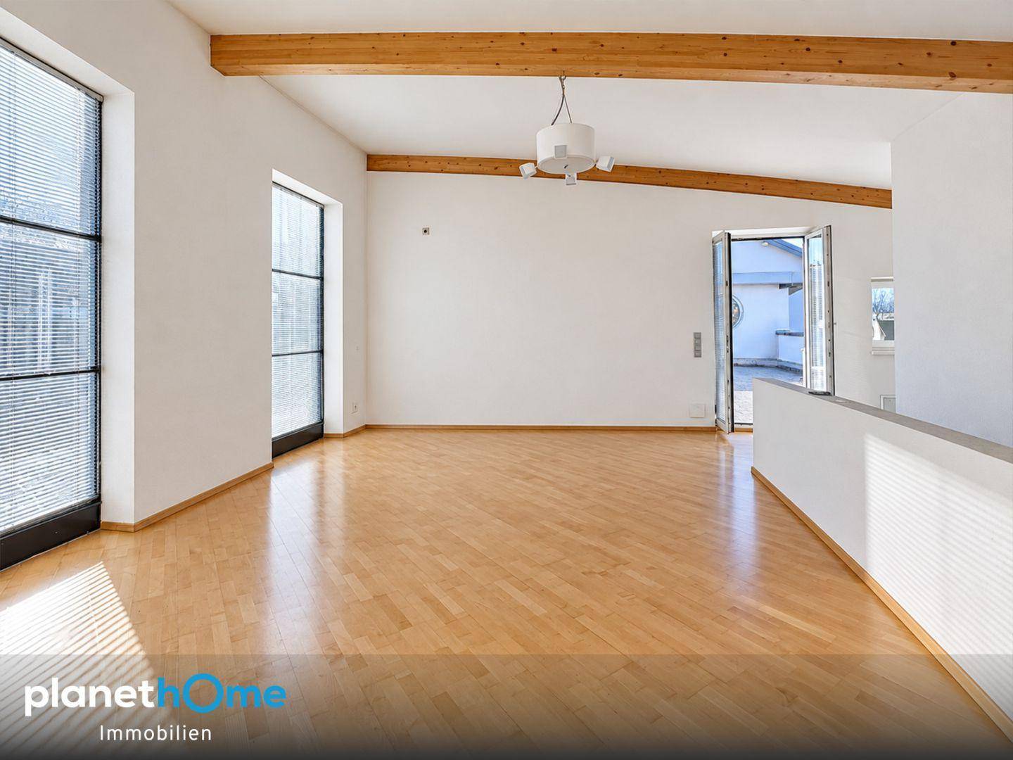 Heller Wohnbereich mit Holzbalken, großen Fenstern und Zugang zu einer Außenterrasse.