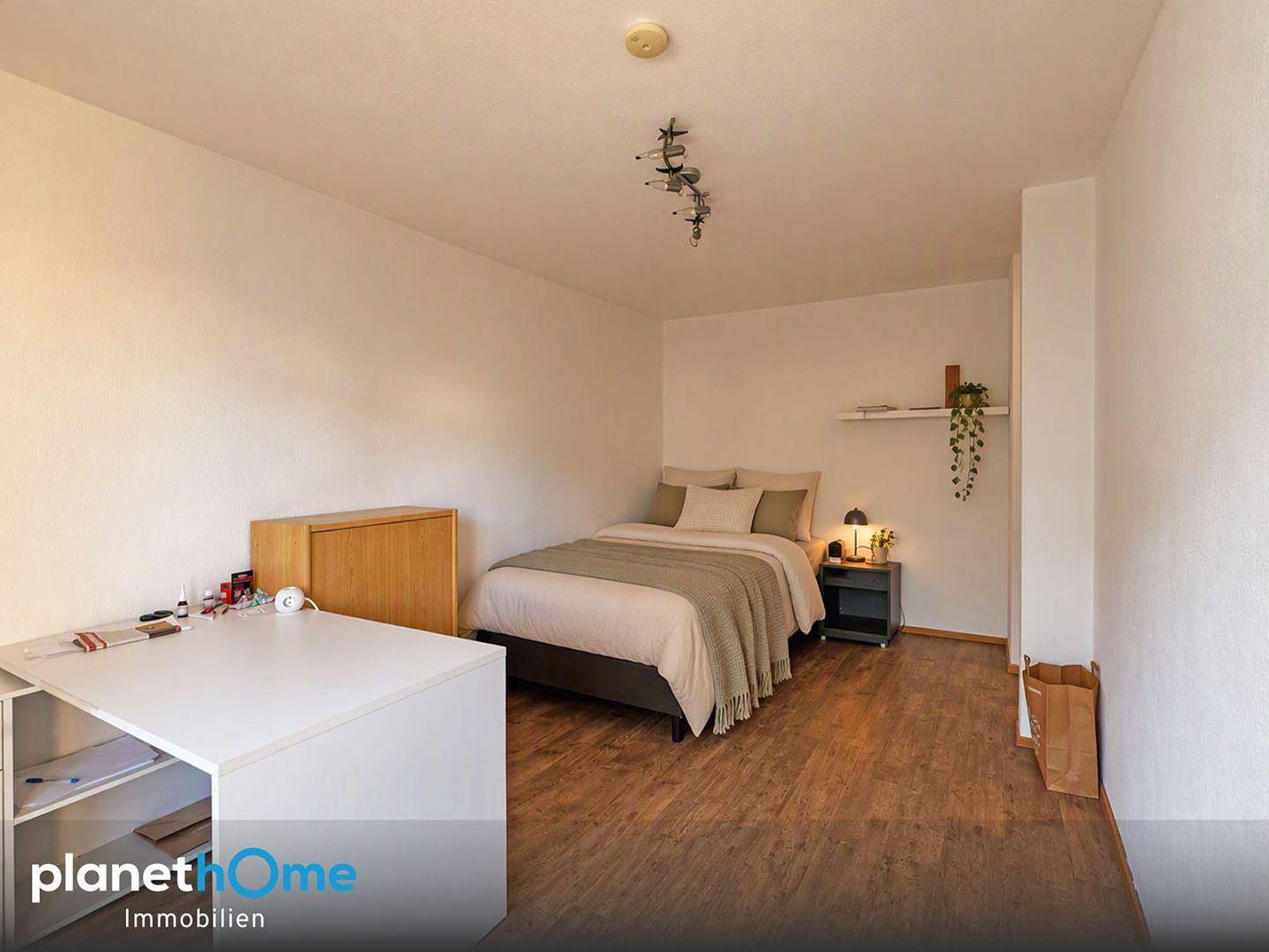 Gemütliches Schlafzimmer mit Holzboden, Bett und einem kleinen Arbeitsbereich.