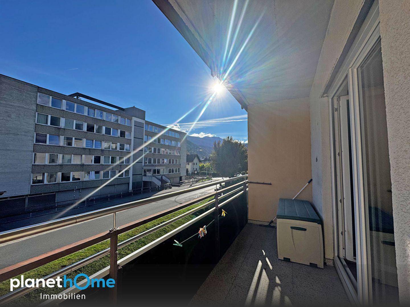 Sonniger Balkon mit Metallgeländer und Blick auf die Straße und umliegende Gebäude.