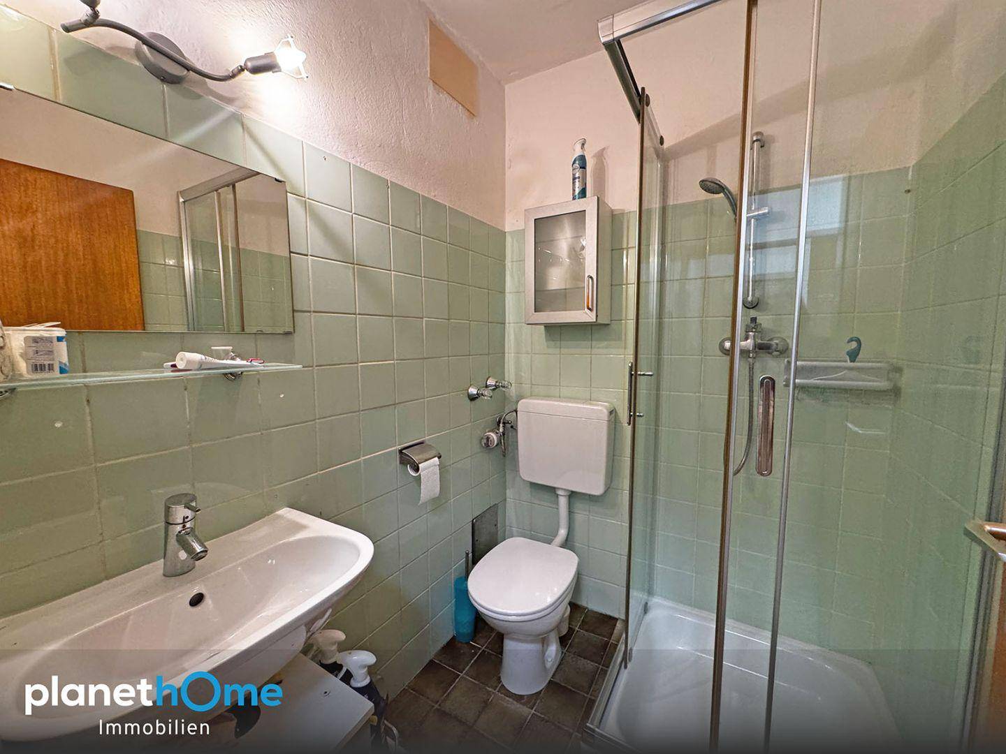 Badezimmer mit grünen Wandfliesen, Dusche, WC und einem einzelnen Waschbecken.