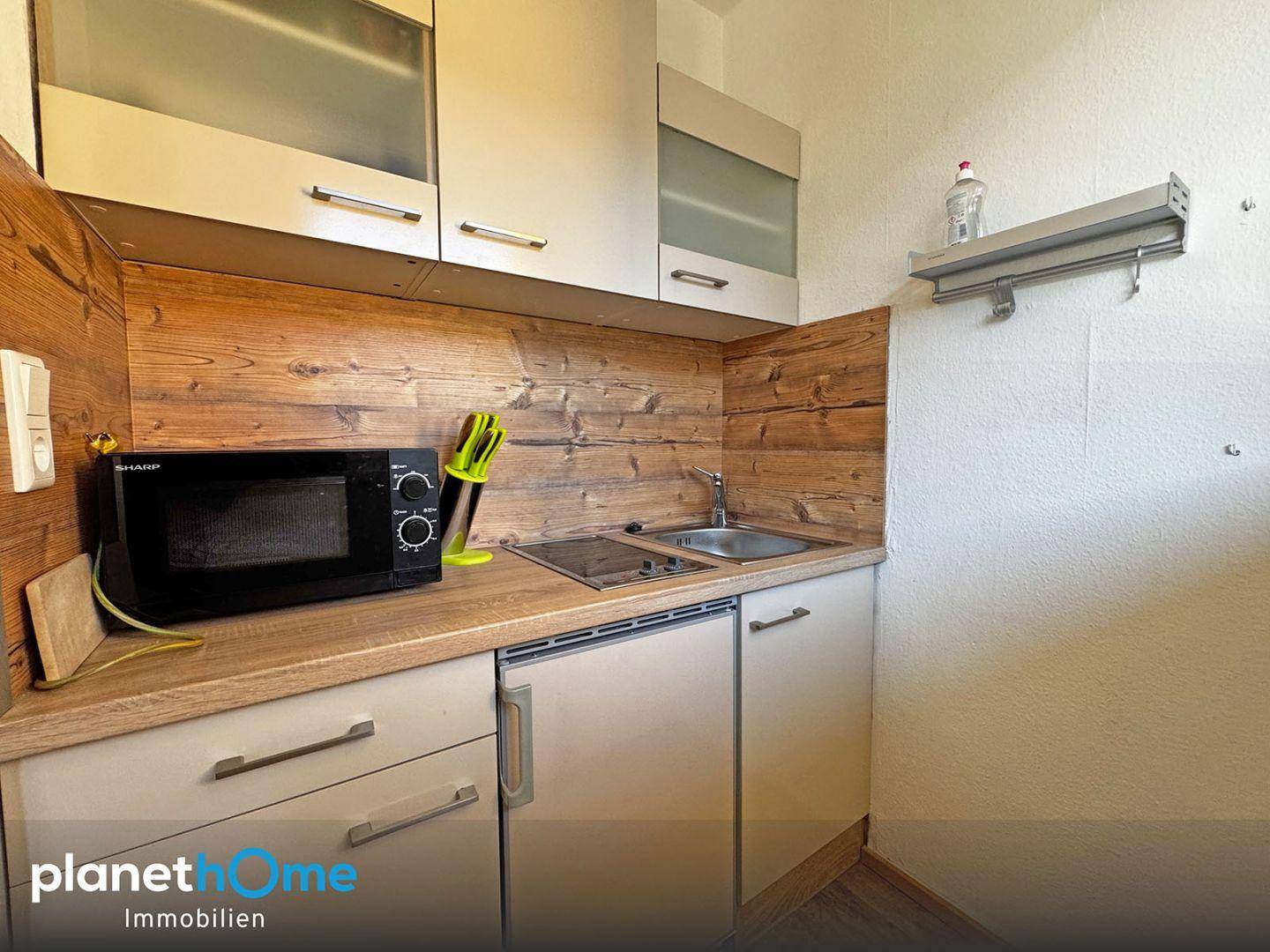 Kleine Küchenzeile mit Mikrowelle, Spüle und rustikaler Holzverkleidung an der Wand.