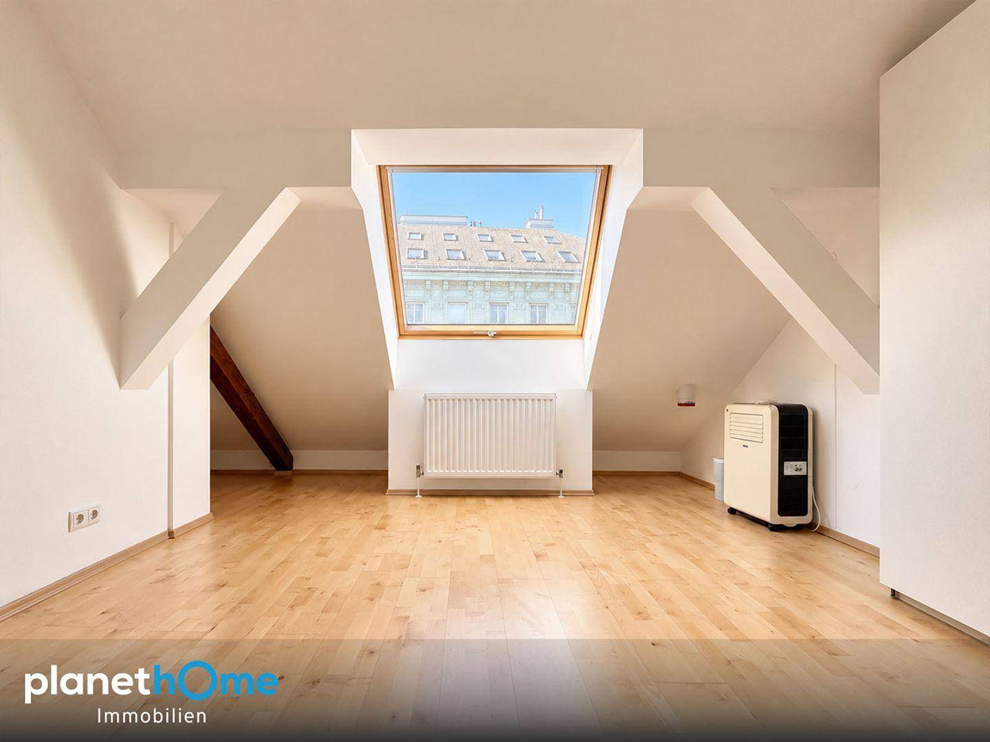 Helles Dachzimmer mit großem Dachfenster, Holzboden und schrägen Wänden, ideal für ein Schlafzimmer.