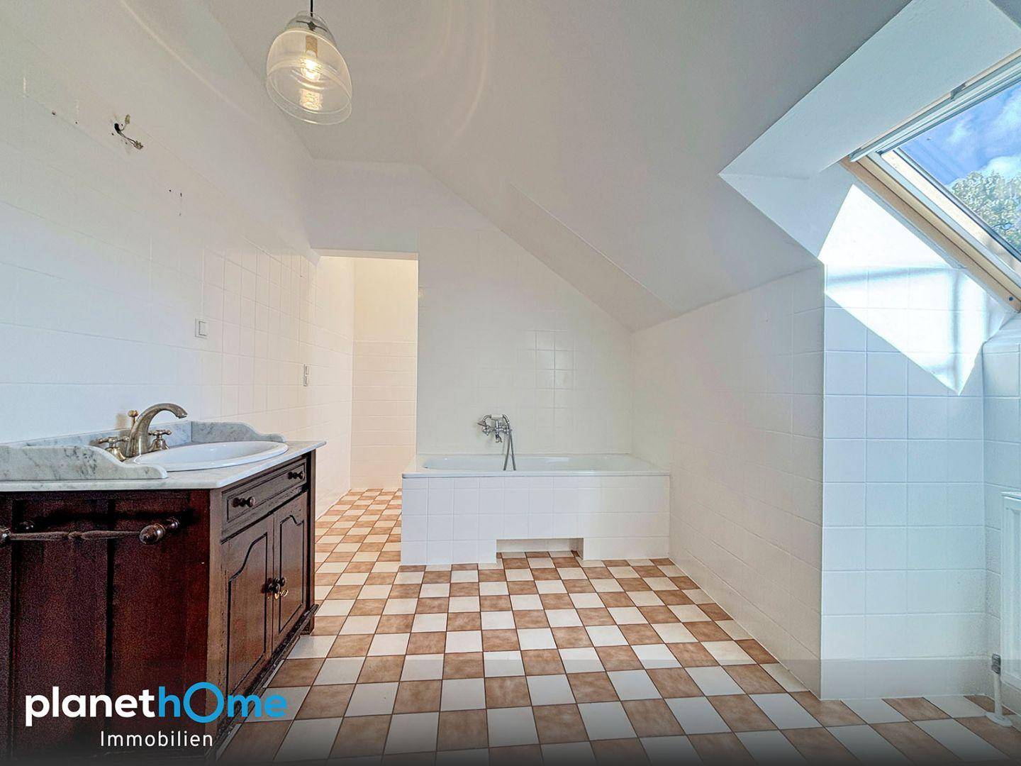 Dachgeschoss-Badezimmer mit Badewanne, Marmorwaschtisch und karierten Fliesen, hell durch Dachfenster.