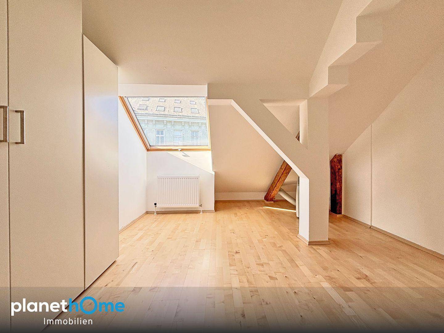 Dachzimmer mit praktischen Einbauschränken, Holzboden und einem großen Dachfenster für viel Licht.