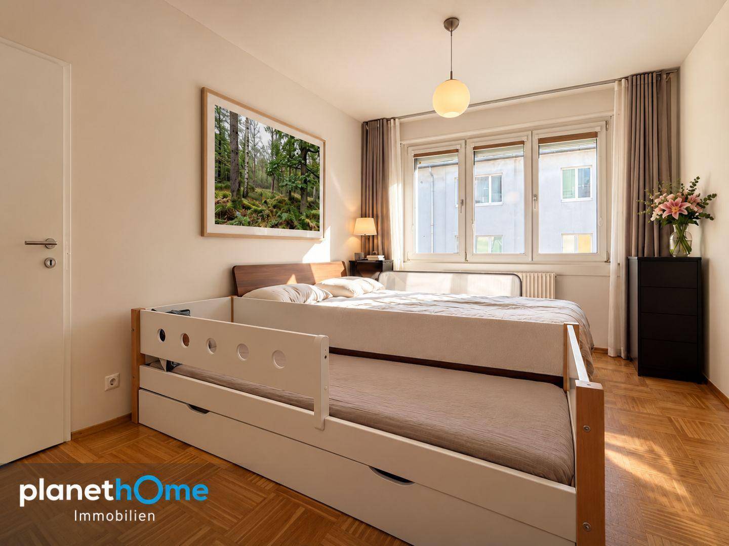 Gemütliches Schlafzimmer mit Holzboden, großem Fenster und einem ausziehbaren Kinderbett.