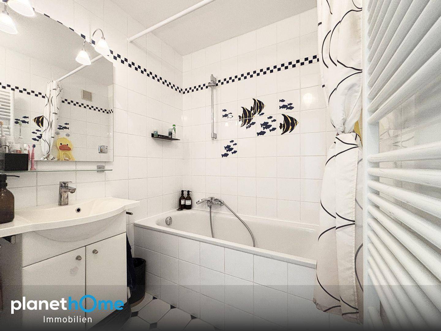 Modern gefliestes Badezimmer mit Badewanne, Waschbecken und einem beheizten Handtuchhalter.