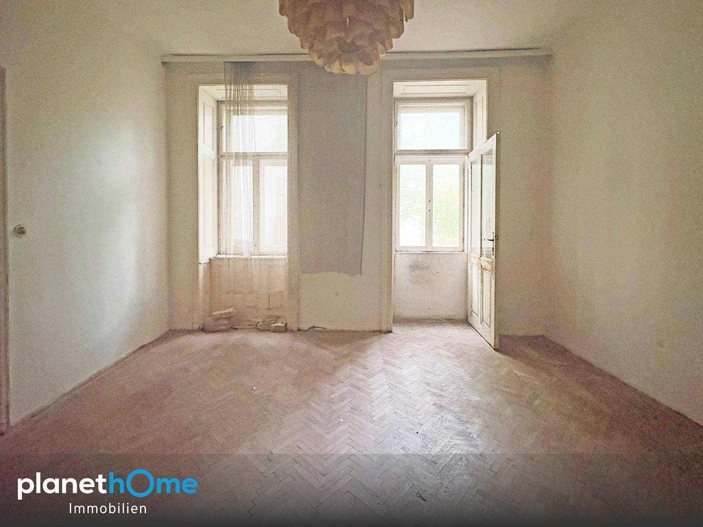 Unrenoviertes Zimmer mit Fischgrätparkett, hohen Fenstern und Renovierungsbedarf.