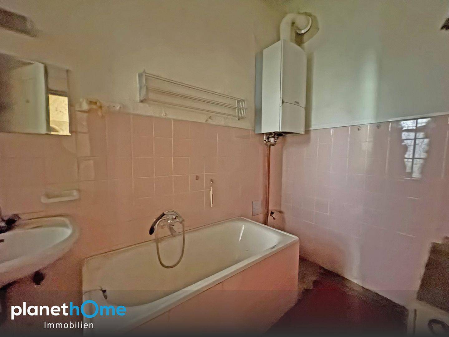 Veraltetes Badezimmer mit rosa Fliesen, Badewanne und Gastherme.