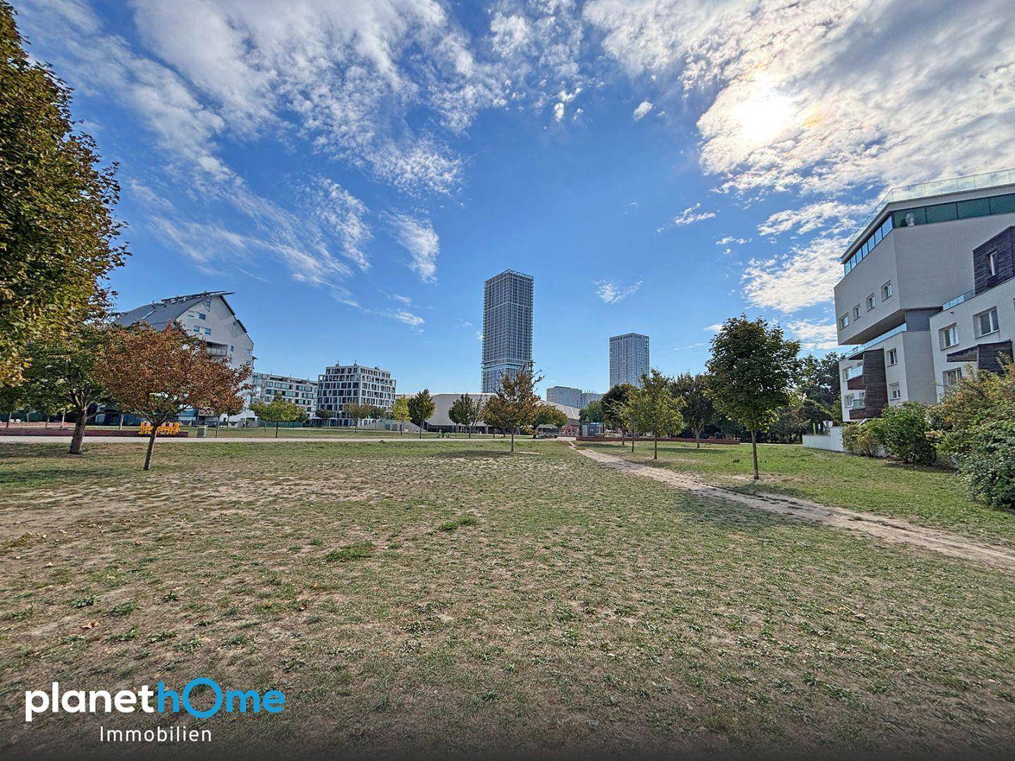 Weitläufige Grünfläche mit Blick auf eine moderne Stadtkulisse und hohe Gebäude am Horizont.