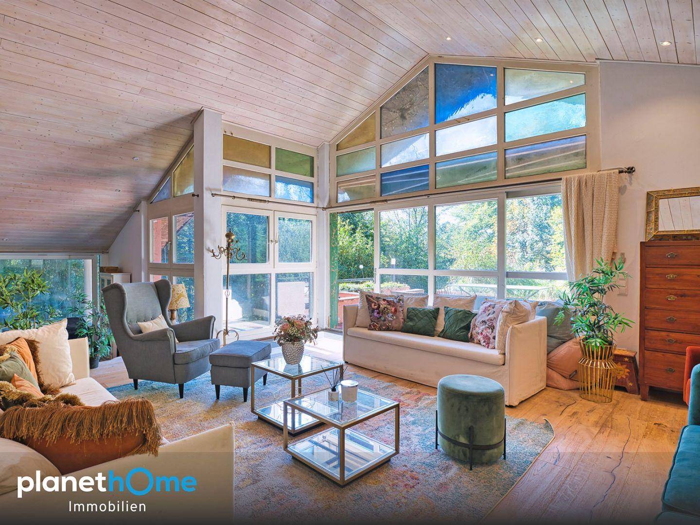Helles Wohnzimmer mit hohen Decken, großen Fenstern und Blick ins Grüne, modern eingerichtet.