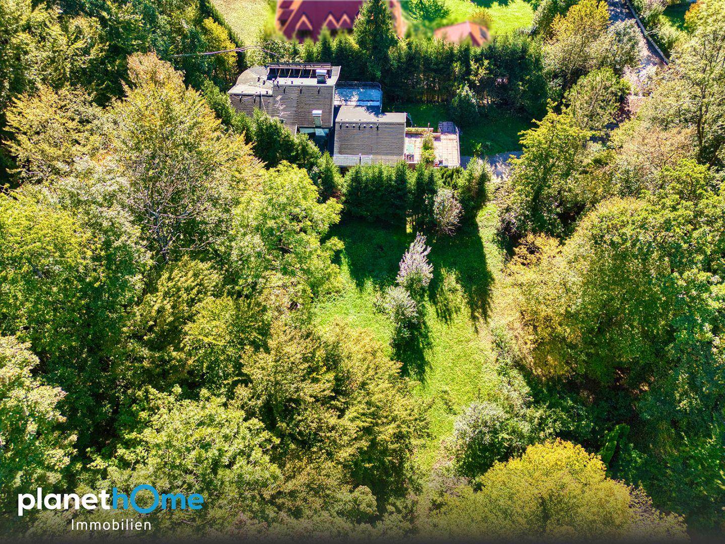 Vogelperspektive eines Hauses, eingebettet in eine grüne Landschaft mit Bäumen und Sträuchern.