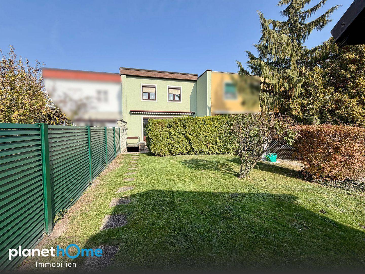 Gepflegter Gartenbereich mit Rasenfläche, Hecke und Blick auf die Rückseite des Hauses.