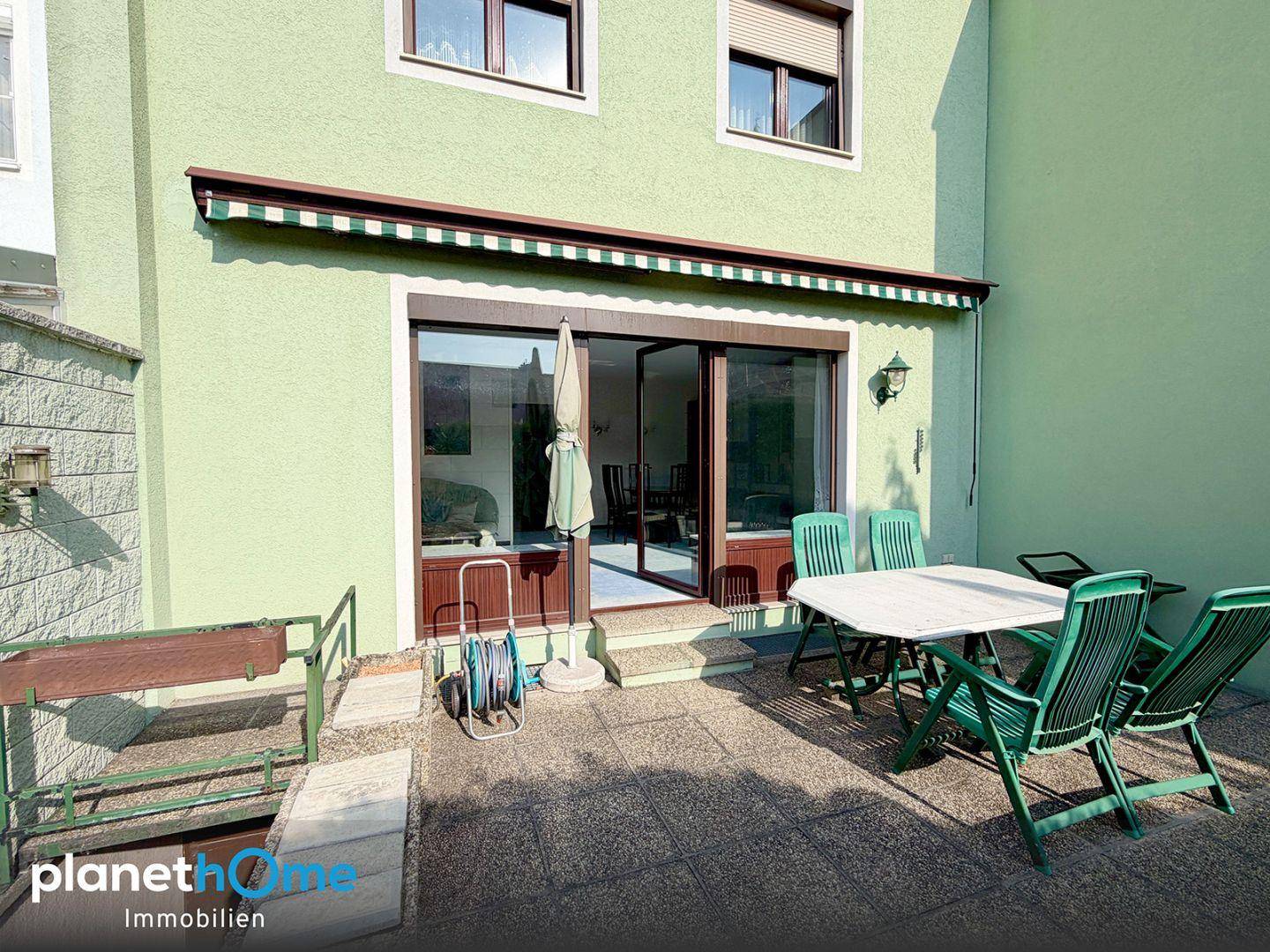 Gepflasterte Terrasse direkt am Haus mit Markise, Gartenmöbeln und Zugang zum Wohnbereich.