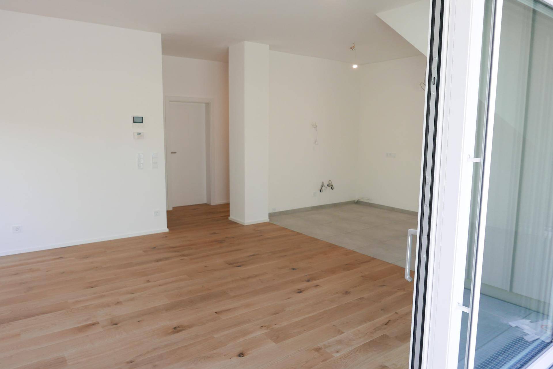 Geräumiger, unmöblierter Raum mit Holzboden und Fliesen, mit Zugang zu einem Balkon oder einer Terrasse.