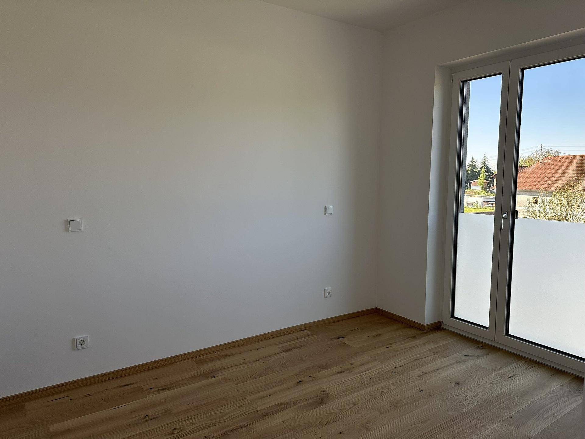 Helles Schlafzimmer mit Holzboden und großem Fenster, bereit zur individuellen Einrichtung und Nutzung.
