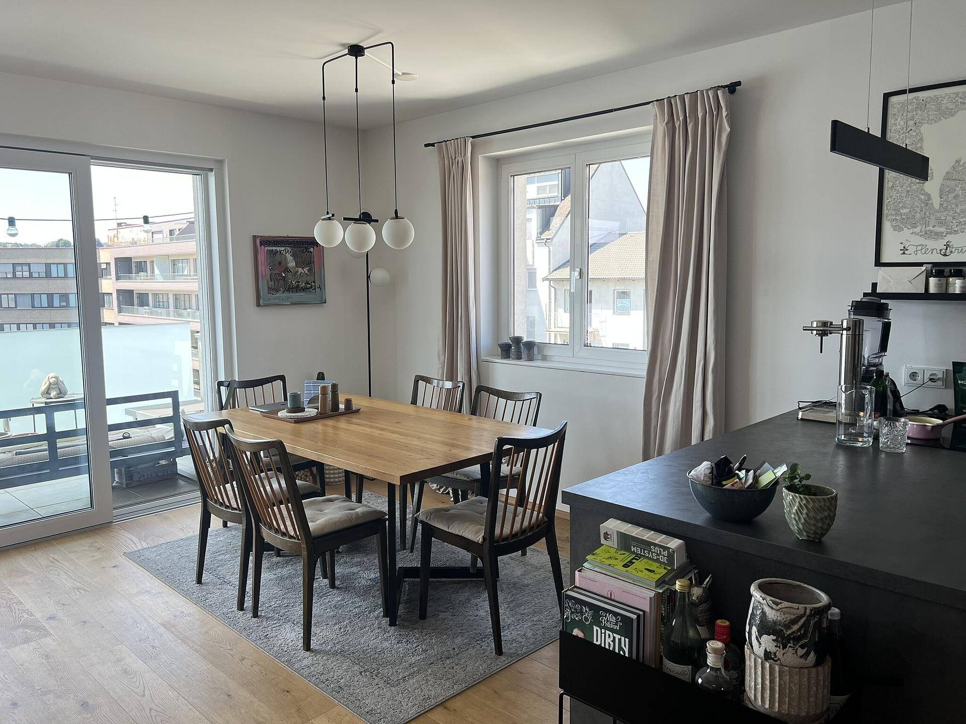 Offener Wohn- und Essbereich mit Holzboden, großem Esstisch und Zugang zum Balkon.
