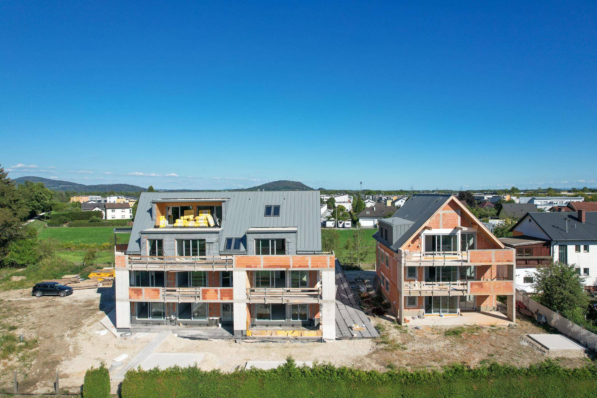 Zwei im Bau befindliche Gebäude mit großen Fensterfronten und Blick ins Grüne.