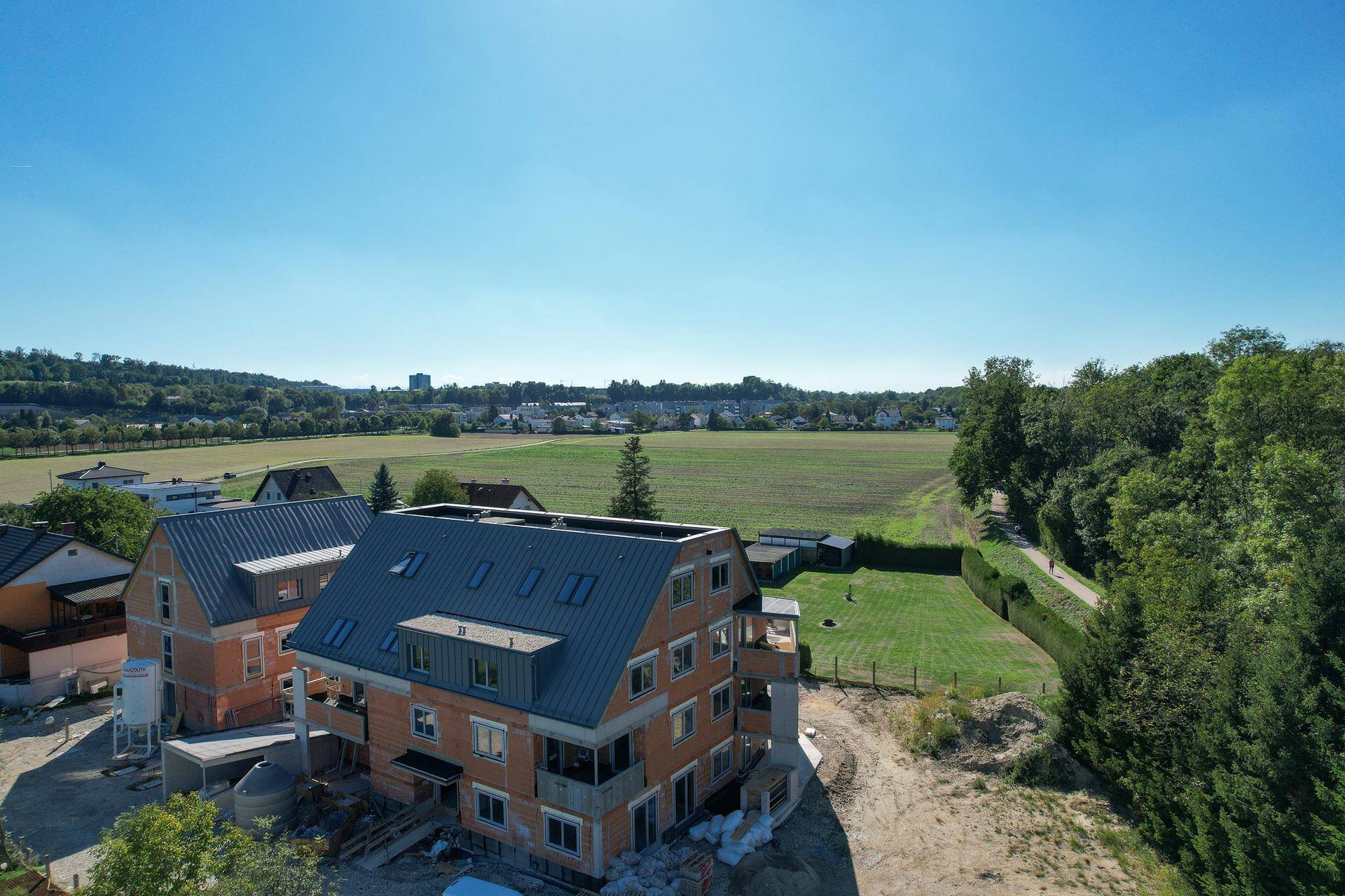 Neubau im Rohbau mit weitem Blick über Felder und eine nahegelegene Ortschaft.