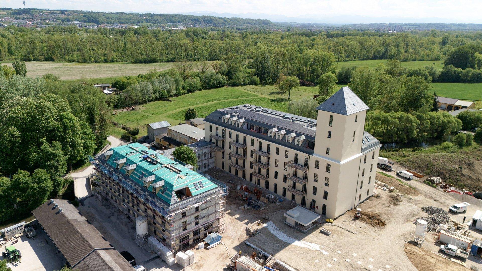 Luftaufnahme einer Baustelle mit zwei Gebäuden und weitreichender grüner Landschaft.