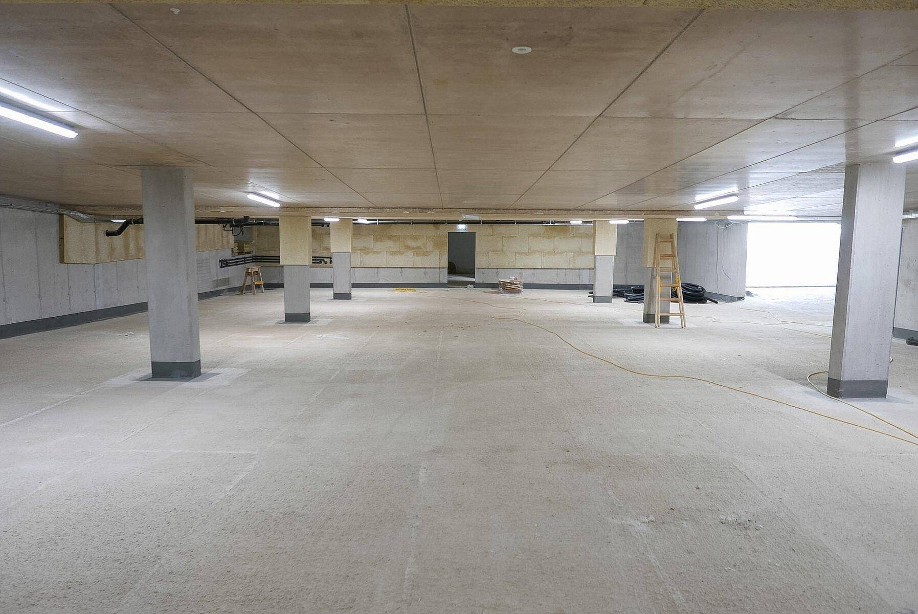 Geräumige und helle Tiefgarage mit Betonboden und Säulen in einem Neubau.