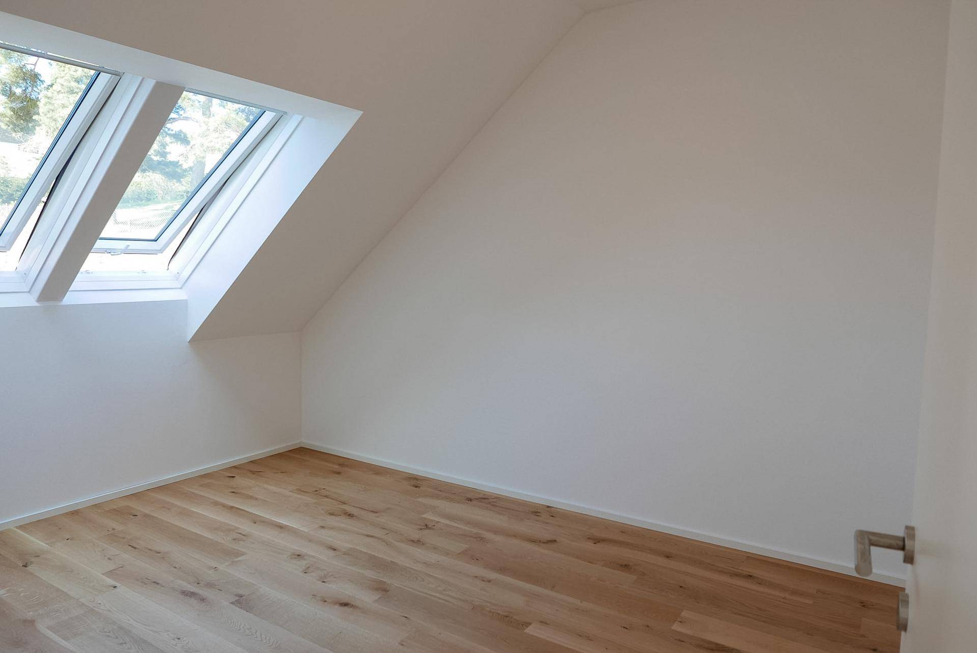 Dachzimmer mit schrägen Wänden, Holzboden und großen Dachfenstern für viel Licht.