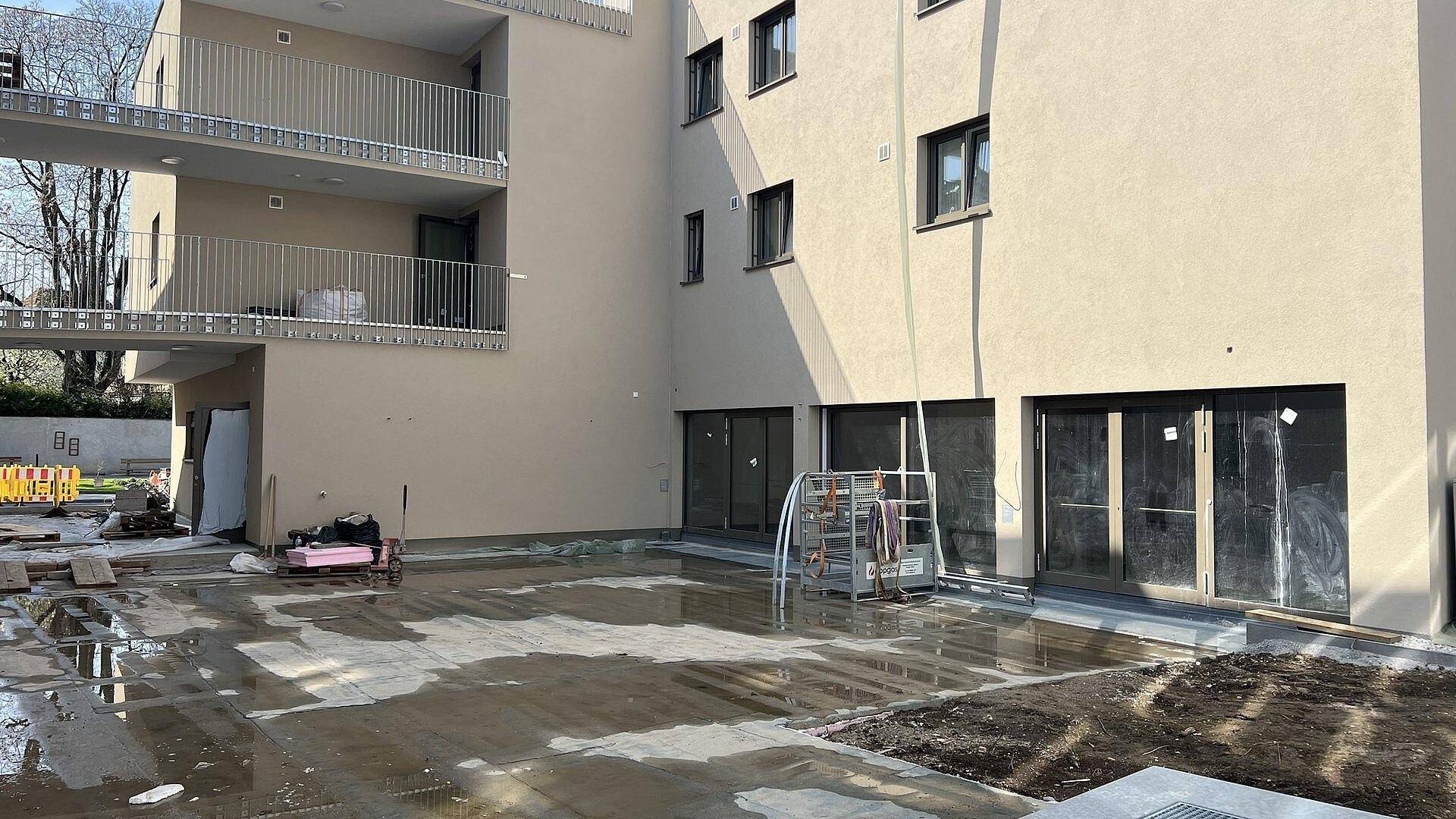 Außenansicht eines Neubaus mit Balkonen und einer im Bau befindlichen, nassen Terrassenfläche.
