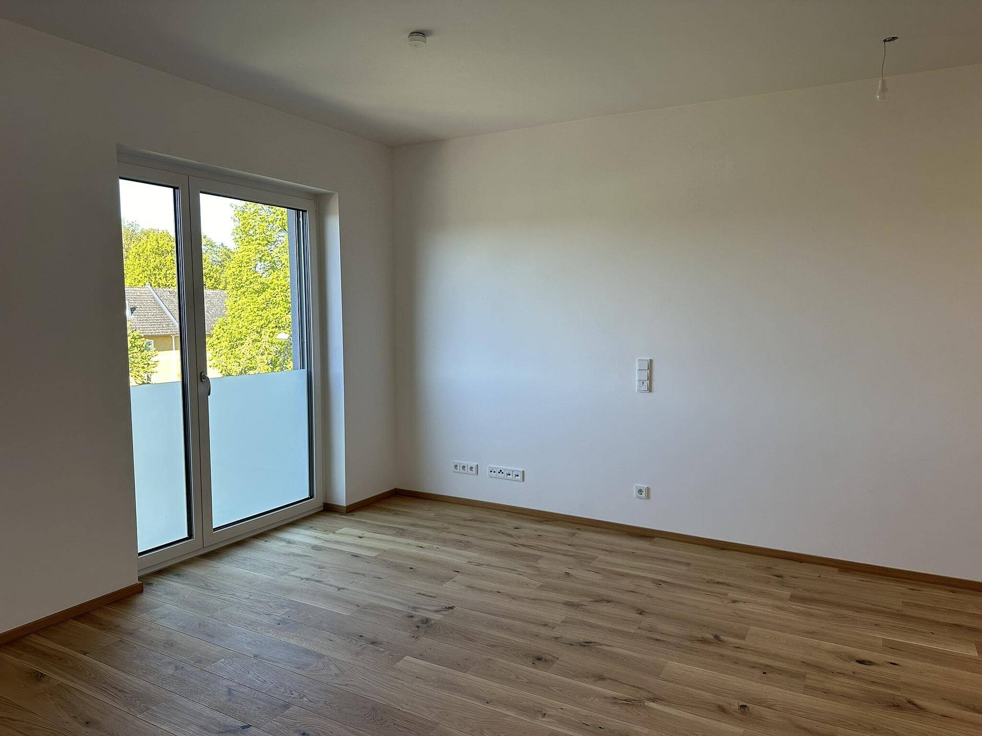 Helles Zimmer mit Holzboden und großem Fenster, ideal als Schlaf- oder Arbeitszimmer nutzbar.