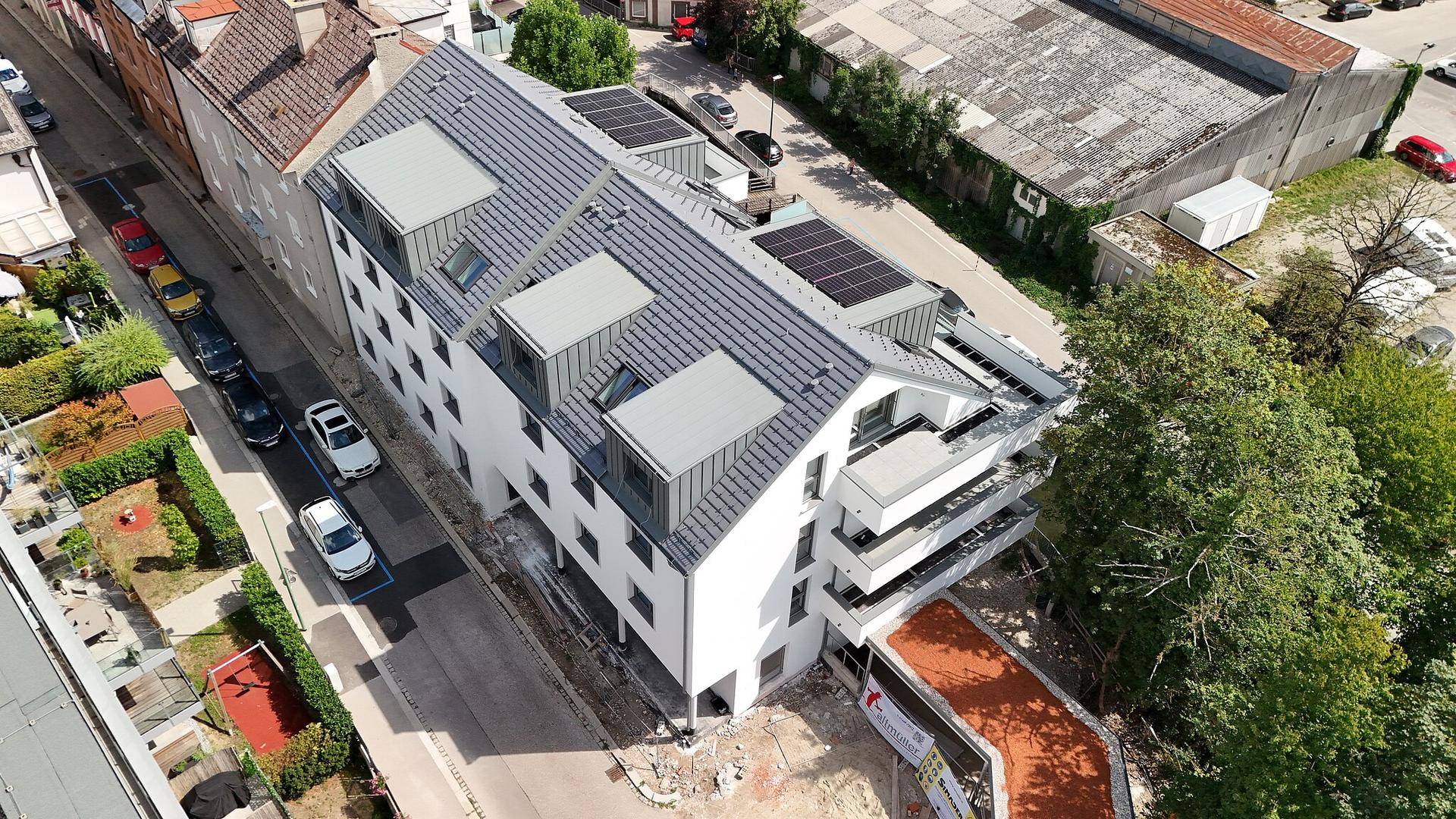 Gesamtansicht des Neubaus mit Solaranlagen auf dem Dach und umliegender Bebauung.