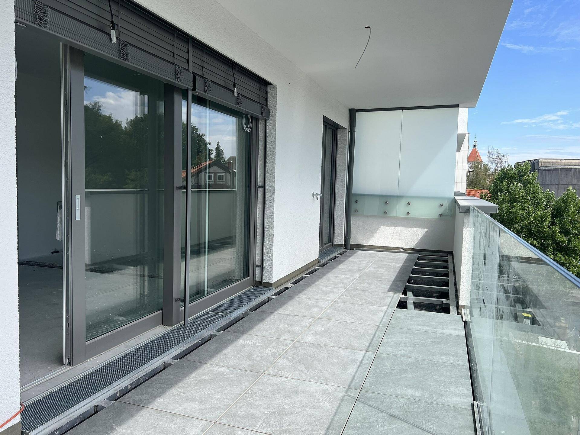Geräumiger Balkon mit Fliesenboden und Glasgeländer, bietet einen Blick auf die Umgebung.