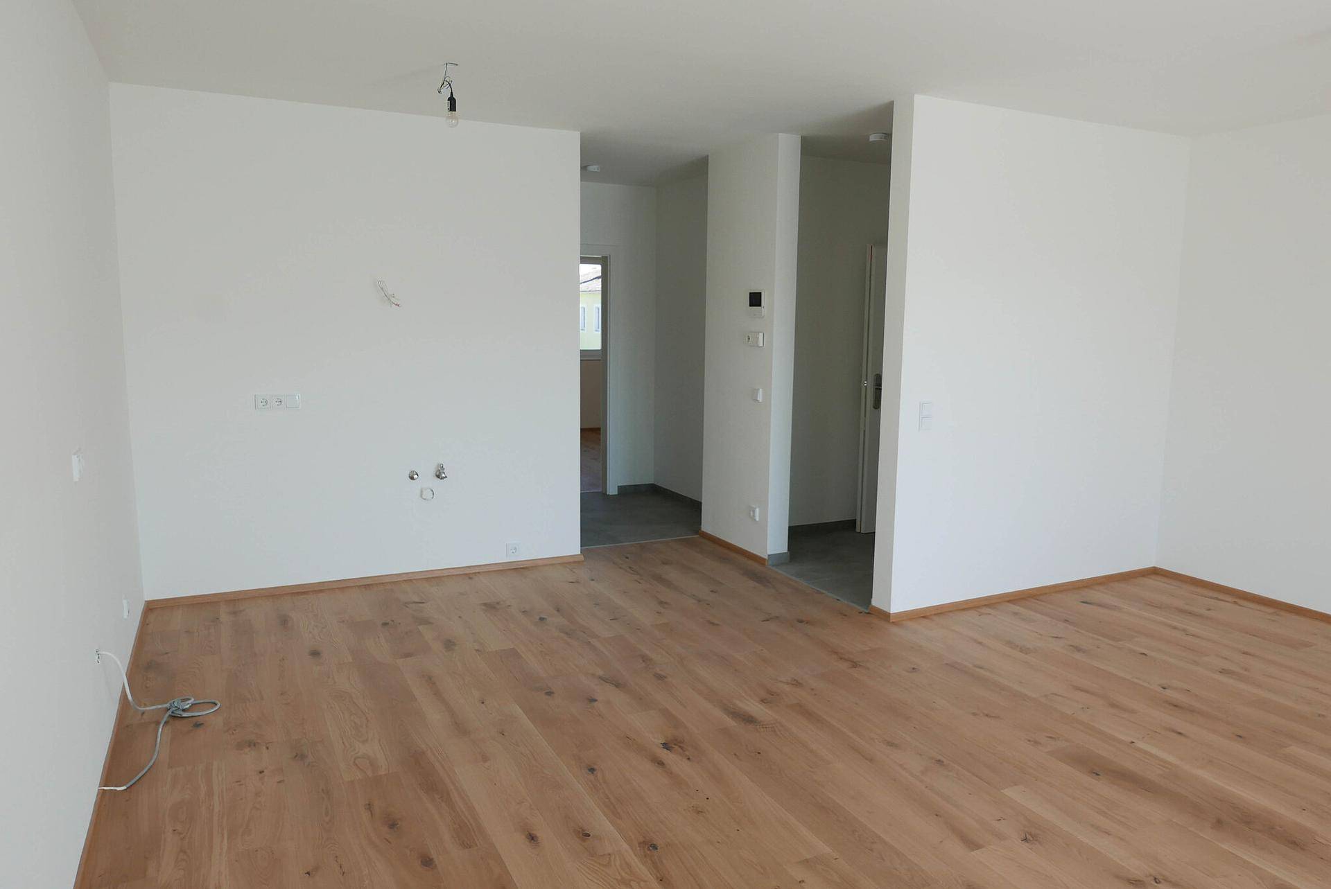 Unmöbliertes Wohnzimmer mit Holzboden, weißen Wänden und offener Raumgestaltung.