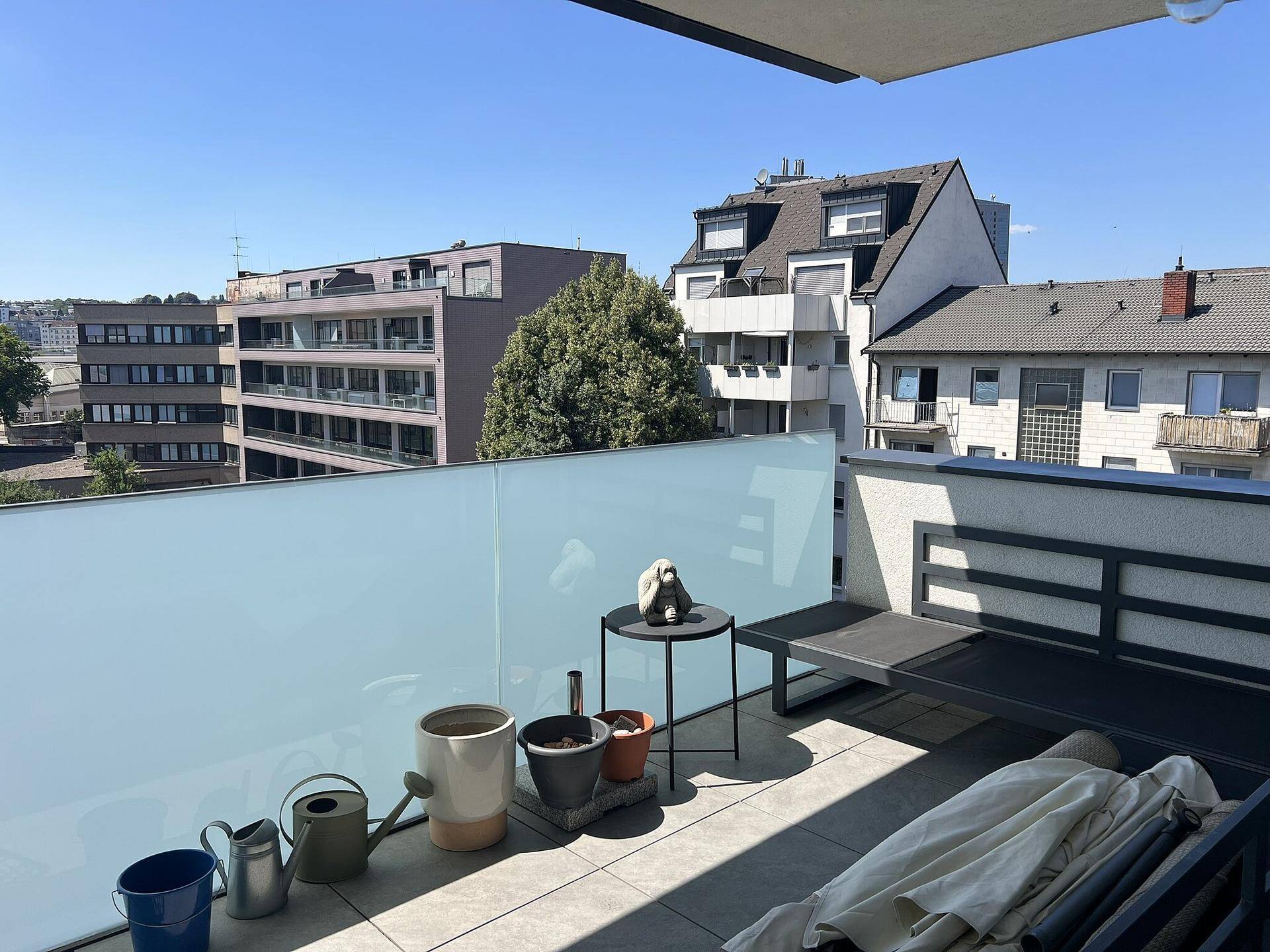 Geräumiger Balkon mit Sitzbank, Pflanzen und Blick auf die umliegenden Gebäude.
