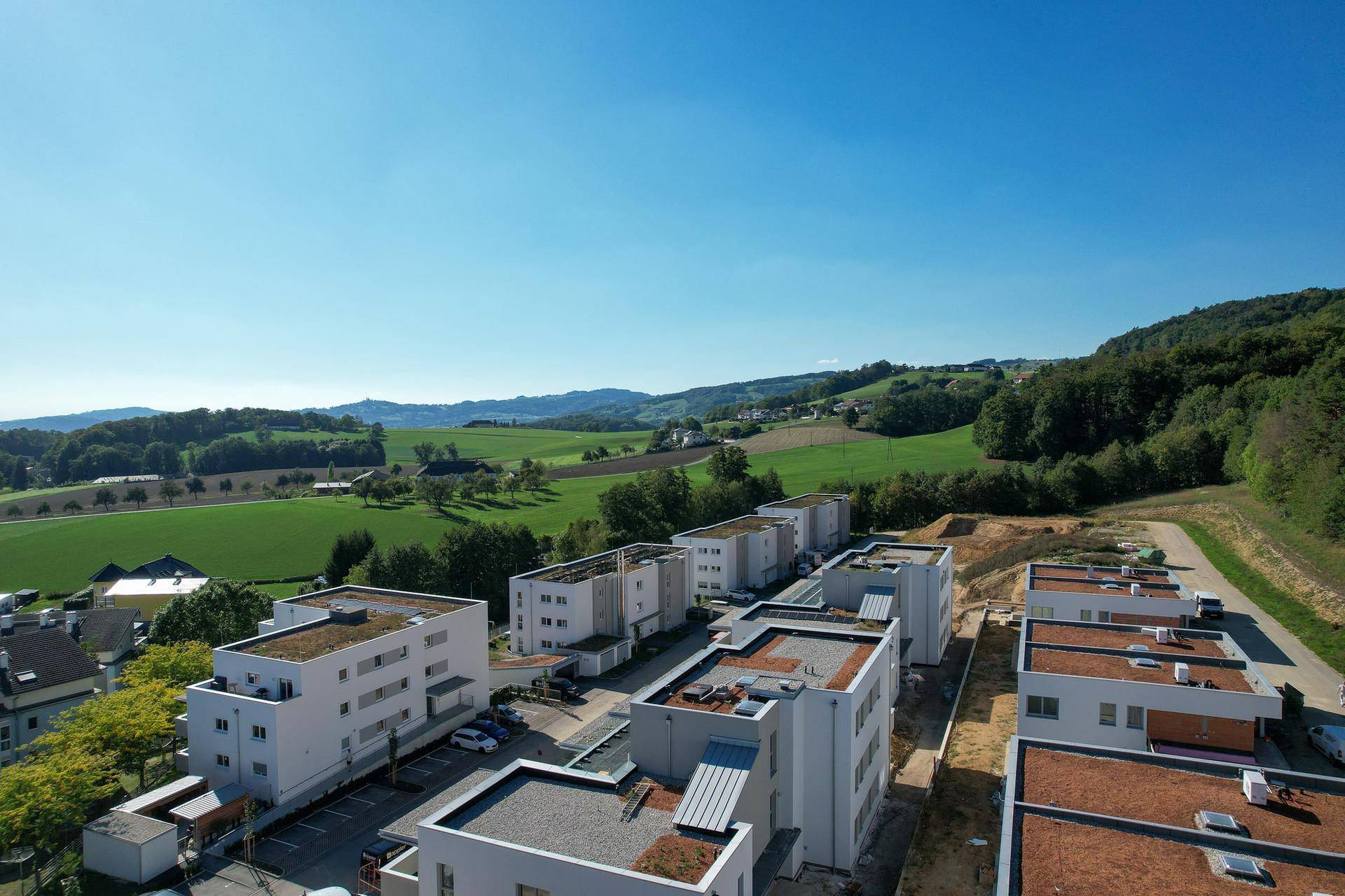 Luftaufnahme einer modernen Wohnanlage mit Flachdächern und viel Grün in ländlicher Umgebung.